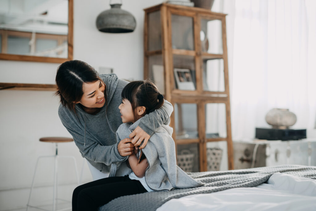 Caring young Asian mother putting a coat on her daughter
